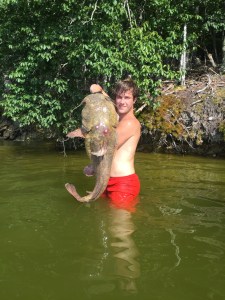 Man in red shorts holding catfish in green water