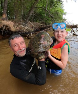 Two people holding large catfish together in water